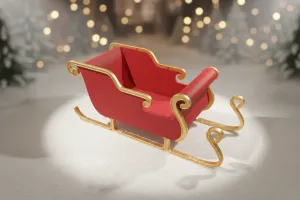 Red and gold decorative sleigh with curved runners placed on a snowy surface. In the softly blurred background, warm lights and snow-covered trees create a cozy winter and holiday atmosphere.
